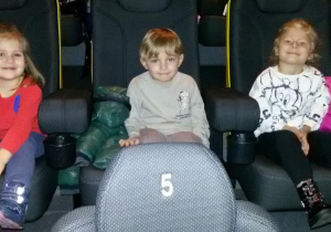 Widok na troje dzieci siedzących na widowni kinowej.